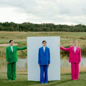Three models in vibrant suits pose outdoors with a minimalist white board.