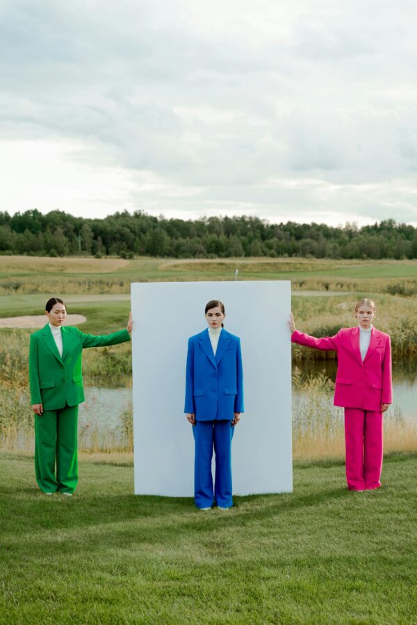 Three models in vibrant suits pose outdoors with a minimalist white board.