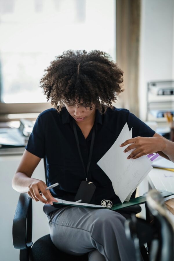 Focused professional woman organizing paperwork at her desk in an office setting during the day.