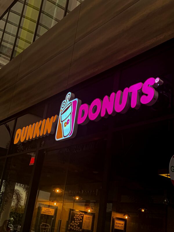 Neon sign of Dunkin' Donuts store illuminating the evening urban scene.