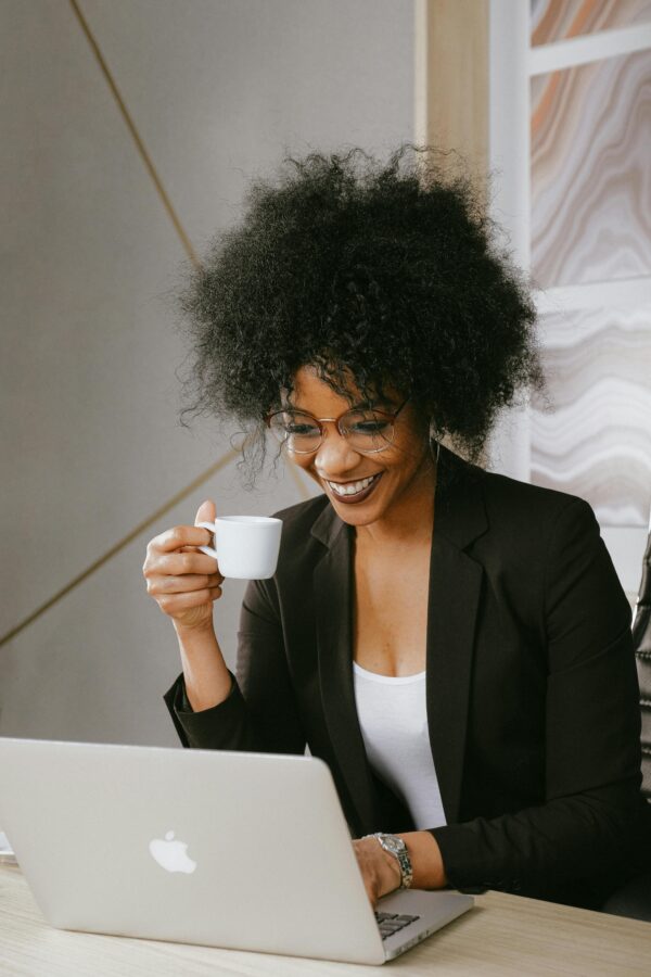 African American woman enjoying coffee while working on a laptop indoors.