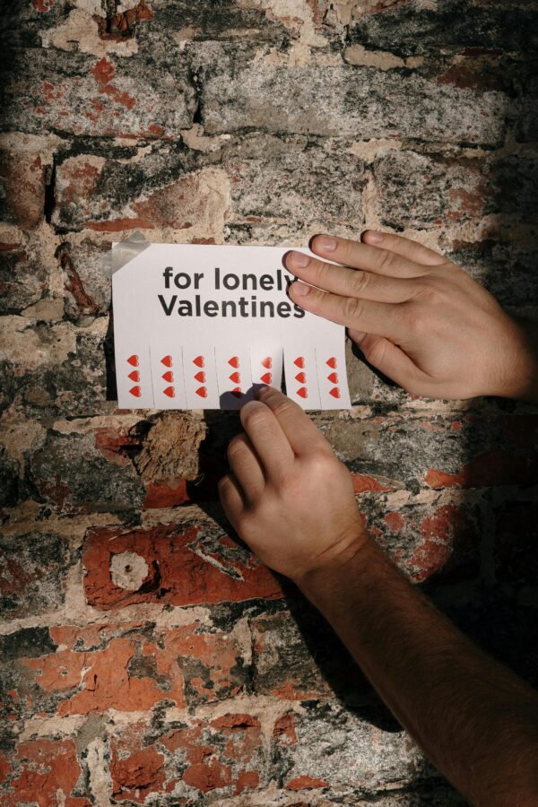 Close-up of hands taping a flyer for lonely Valentines on a brick wall.