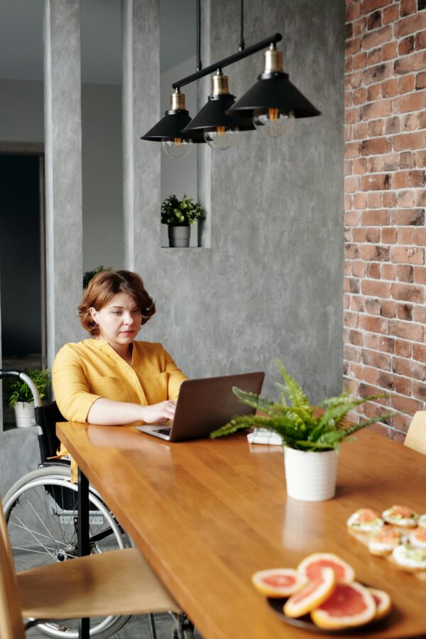 Businesswoman in a wheelchair working from home on a laptop, enjoying a meal.