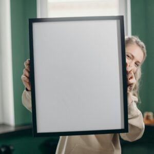 A woman indoors holding a blank photo frame, perfect for mockup or customization.