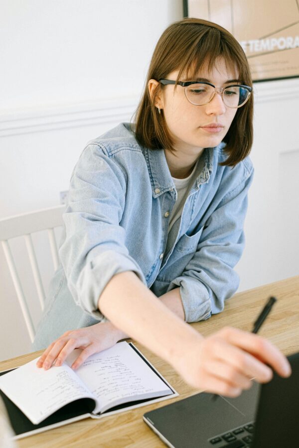 A focused young woman taking notes in a home office with a laptop.
