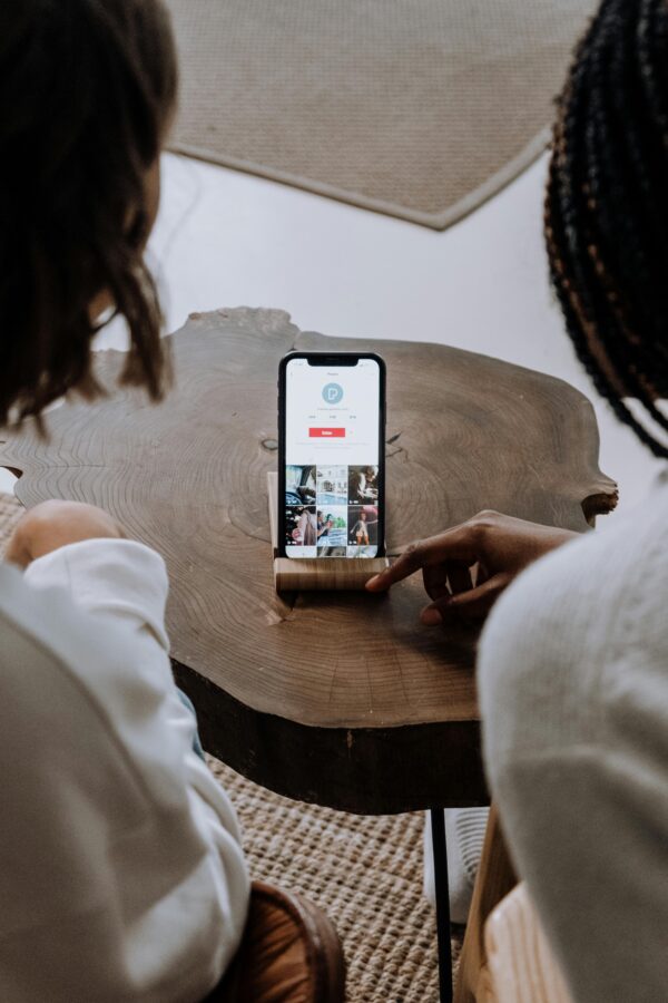 Two individuals engage with a smartphone on a wooden table indoors, highlighting technology in a casual setting.