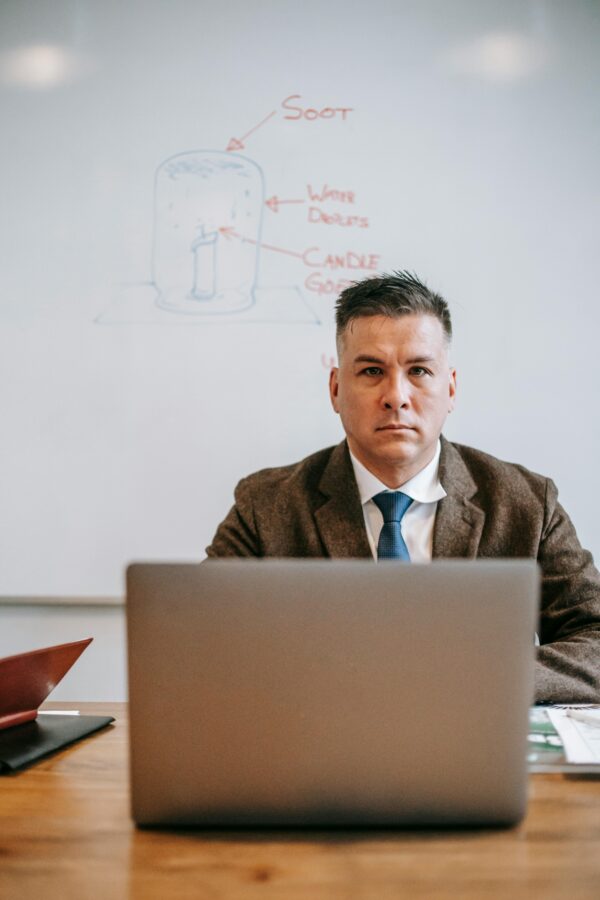 Professional man in formal attire using a laptop in an office setting with whiteboard.