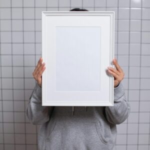An unrecognizable individual holding an empty frame, standing against a tiled background, merged with a minimalist style.