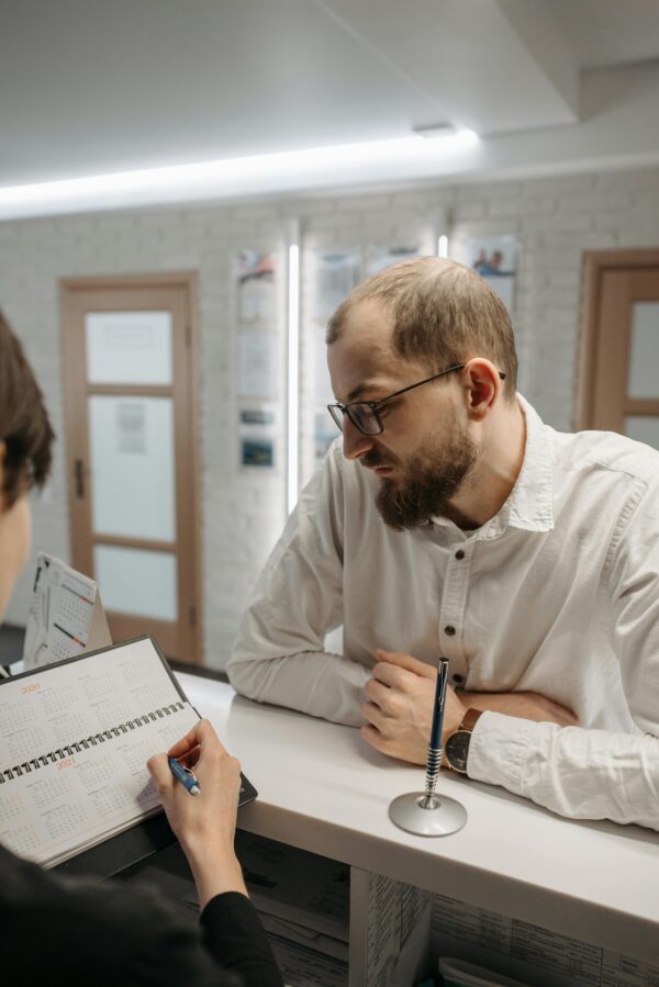 A thoughtful man leaning on a reception counter while discussing plans indoors.