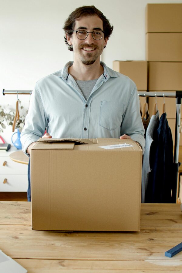 A cheerful businessman holding a package in a modern indoor workspace, signifying small business and entrepreneurship.